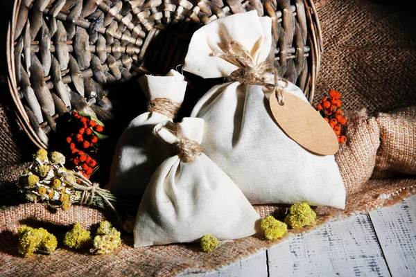 Bolsa de bolsita textil con flores secas, hierbas y bayas sobre mesa de madera, sobre fondo de saco —  Fotos de Stock