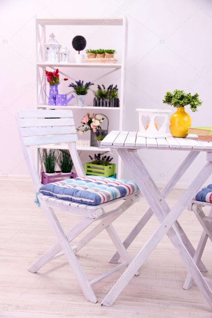 Garden chair and table with flowers on shelves on white background