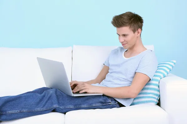 Cara mentira no sofá com laptop no fundo azul — Fotografia de Stock