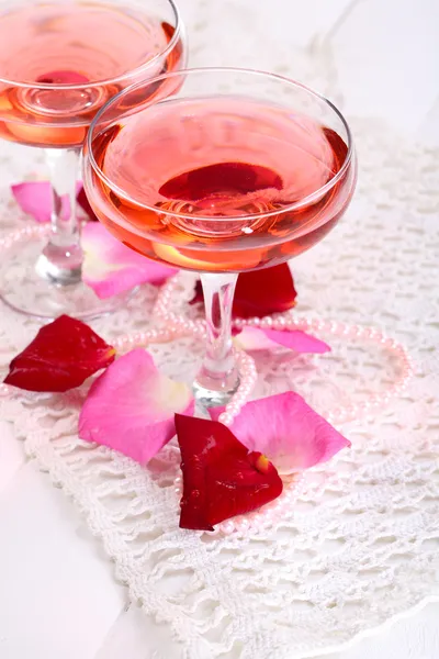 Состав с розовым игристым вином в стаканах и лепестками роз изолирован на белом — стоковое фото