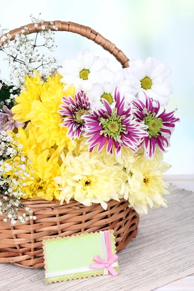 Schöne Chrysanthemenblumen im Weidenkorb auf dem Tisch auf hellem Hintergrund — Stockfoto