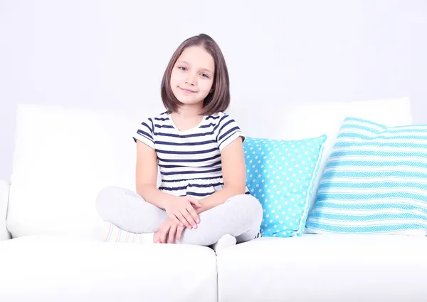 Hermosa niña sentada en el sofá, en el fondo interior de casa —  Fotos de Stock