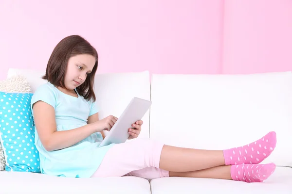Menina bonita sentada no sofá com tablet, em casa fundo interior — Fotografia de Stock
