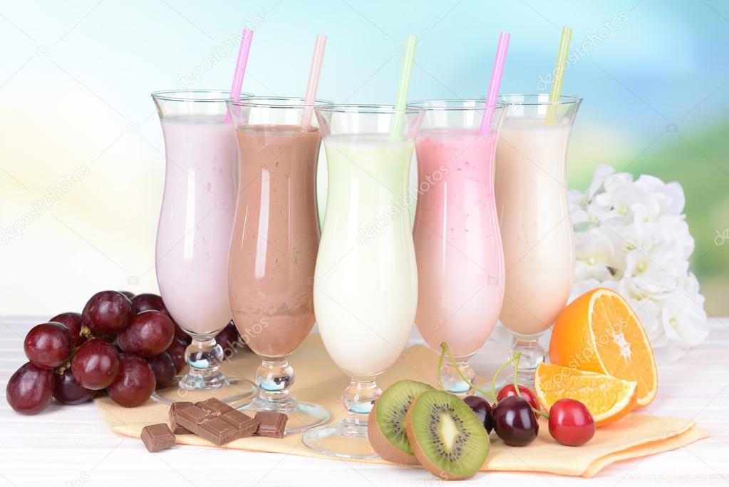Milk shakes with fruits on table on light blue background