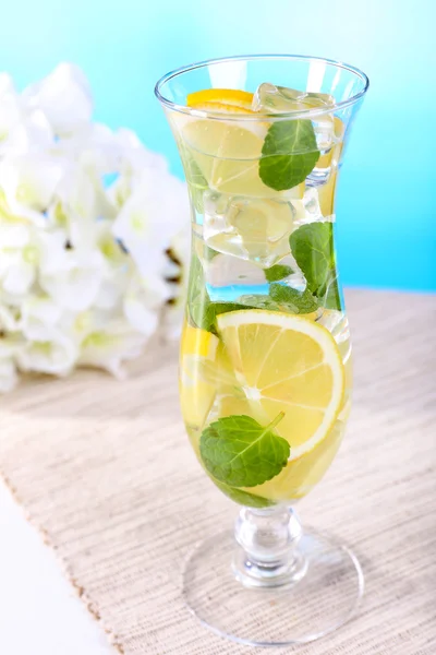 Glass of cocktail with lemon and mint on table on light blue background — Stock Photo, Image