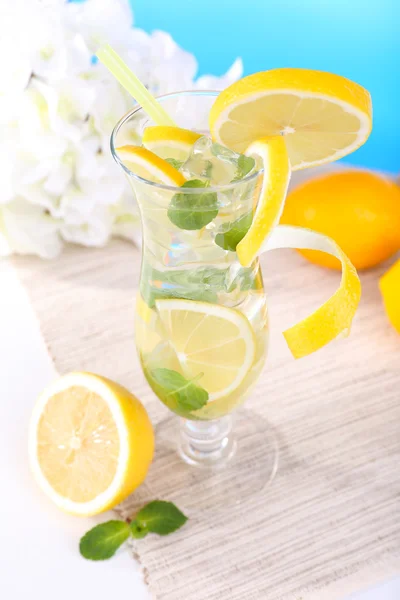 Glass of cocktail with lemon and mint on table on light blue background — Stock Photo, Image