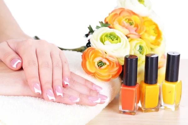 Hermosas manos de mujer con manicura francesa y flores en la mesa sobre fondo blanco — Foto de Stock