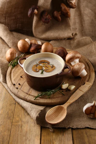 Composition with mushroom soup in pot, fresh and dried mushrooms, on wooden table, on sackcloth background — Stock Photo, Image