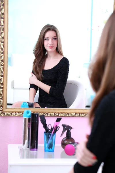 Joven hermosa mujer sentada frente al espejo en la habitación — Foto de Stock