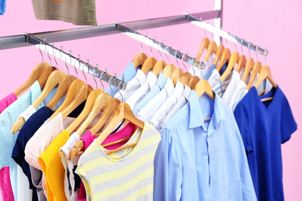 Different clothes on hangers, on pink background — Stock Photo, Image