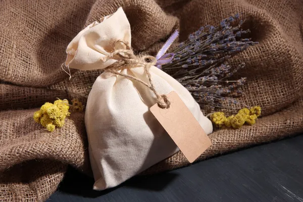Bustina di tessuto con fiori secchi, erbe su tavola di legno, su fondo di sacco — Foto Stock
