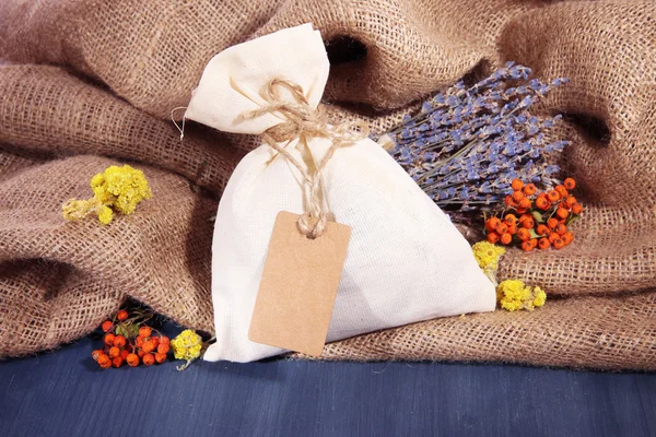 Bolsa de bolsita textil con flores secas, hierbas y bayas sobre mesa de madera, sobre fondo de saco —  Fotos de Stock