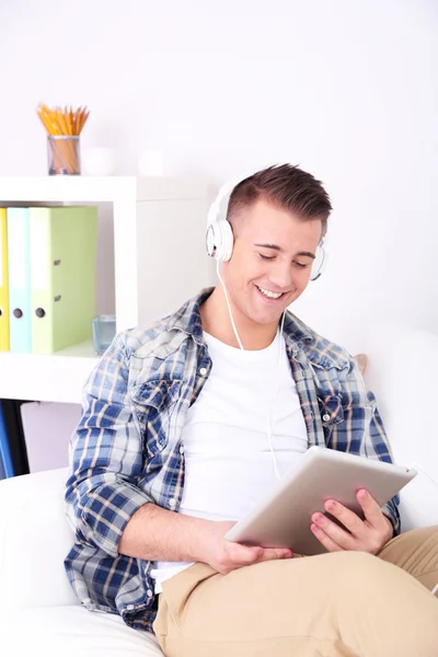 Bonito jovem sentado no sofá e ouvindo música no quarto — Fotografia de Stock