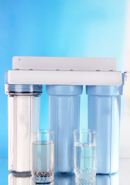 Sistem filter untuk pengolahan air dengan gelas air bersih dan kotor pada latar belakang biru — Stok Foto
