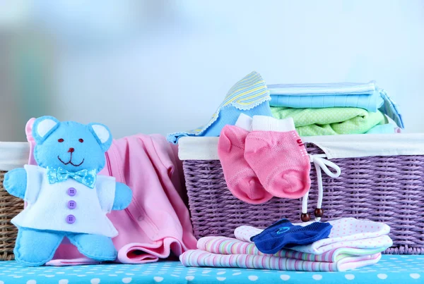 Pile of baby clothes  in basket, on table on color background — Stock Photo, Image