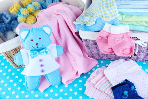 Pile of baby clothes  in basket, on table on color background — Stock Photo, Image