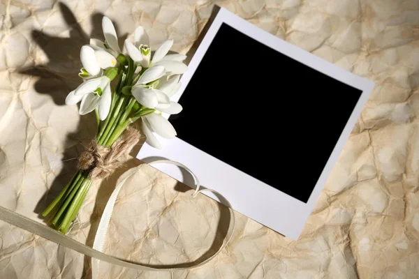 Beautiful bouquet of snowdrops and empty photo paper on old paper background — Stock Photo, Image