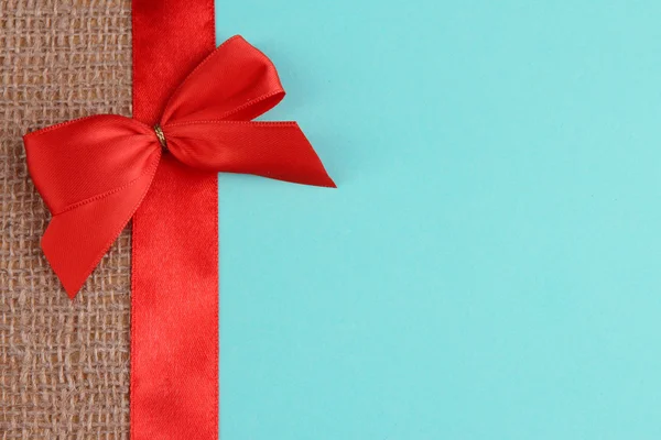 Sackcloth with color ribbon and bow on color paper background — Stock Photo, Image