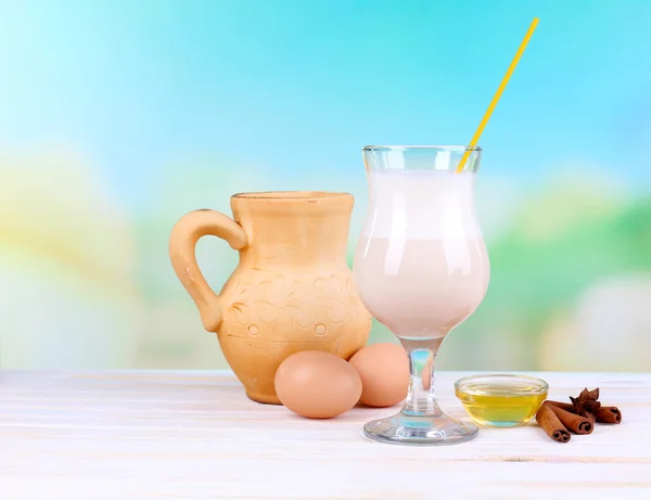 Eggnog with milk and eggs on wooden table and natural background