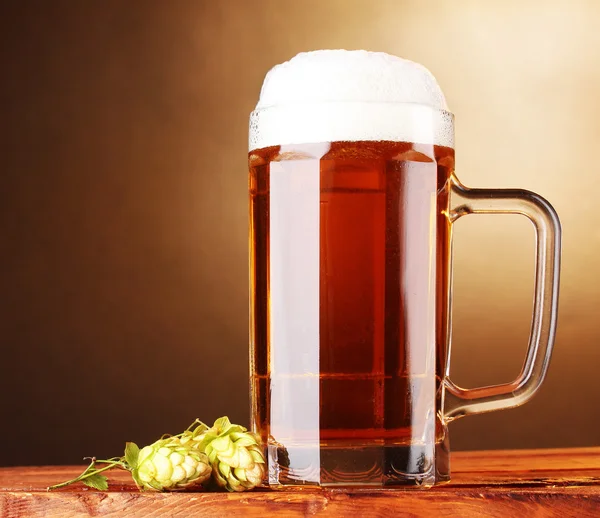 Beer mug and green hop on wooden table on brown background — Stock Photo, Image