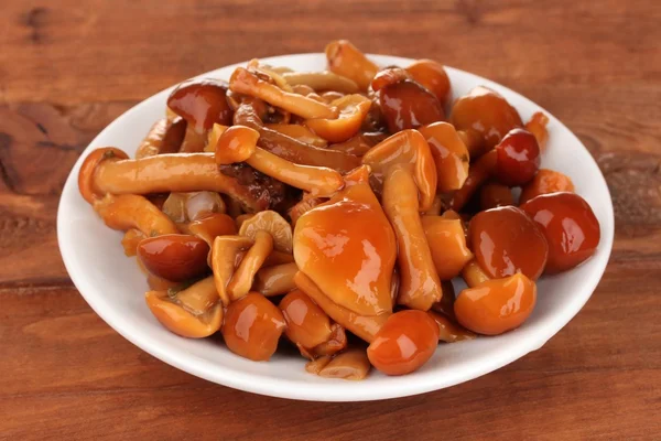 Marinated mushrooms in saucer on wooden table — Stock Photo, Image