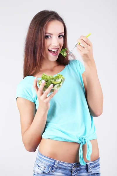 Beautiful girl with fresh salad on grey background — Stock Photo, Image