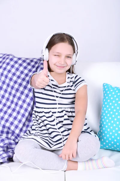 Hermosa niña sentada en el sofá y escuchando música, en el fondo interior de casa —  Fotos de Stock