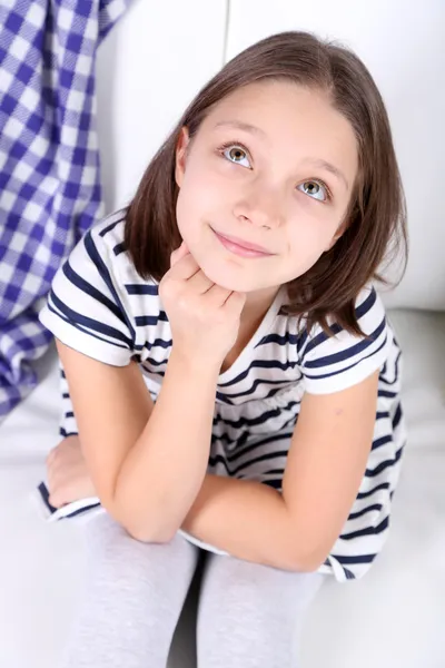 Beautiful little girl sitting on sofa, on home interior background — Stock Photo, Image