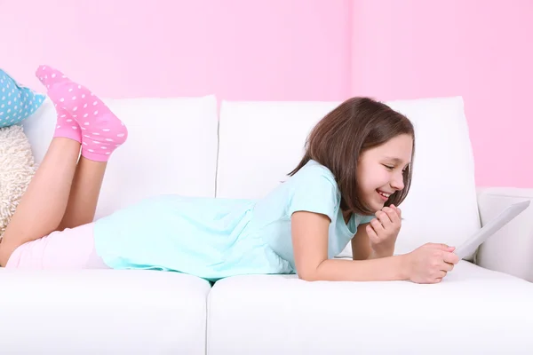 Schöne kleine Mädchen auf dem Sofa mit Tablet, zu Hause im Inneren Hintergrund — Stockfoto