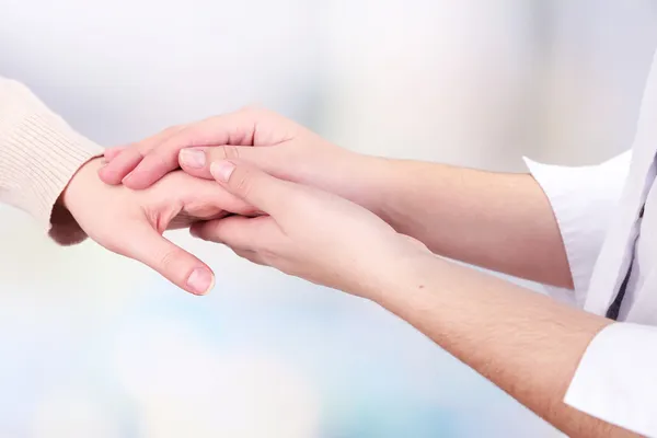 Medical doctor holding hand of patient, on light background — Stock Photo, Image