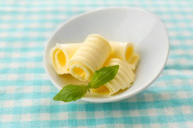Fesleğenli mavi masa örtüsü üzerinde kase taze tereyağı bukleler