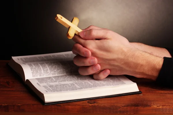 Manos sosteniendo la cruz de madera sobre la sagrada Biblia rusa abierta sobre fondo gris — Foto de Stock