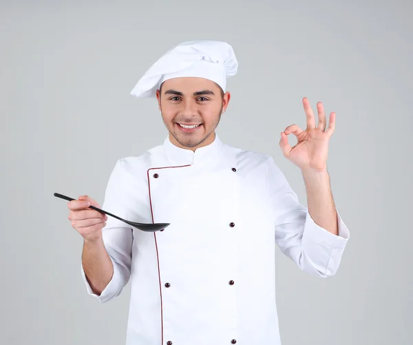 Chef profesional en uniforme blanco y sombrero, sobre fondo gris — Foto de Stock