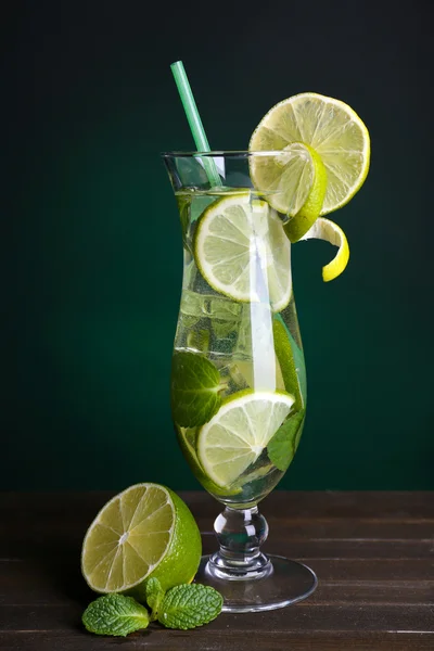 Verre de cocktail avec citron vert et menthe sur la table sur fond vert foncé — Photo