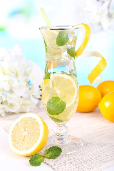 Ποτήρι κοκτέιλ με λεμόνι και δυόσμο στο τραπέζι σε γαλάζιο φόντο — Φωτογραφία Αρχείου