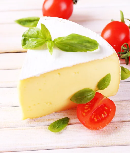 Tasty Camembert cheese with basil and tomatoes, on wooden table — Stock Photo, Image