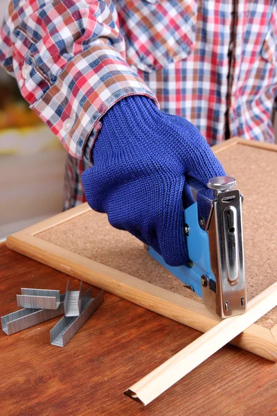 Fastening wooden lath and cork board using construction stapler on bright background
