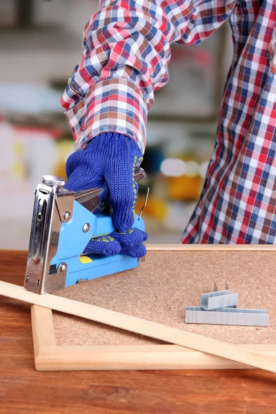 Fastening wooden lath and cork board using construction stapler on bright background