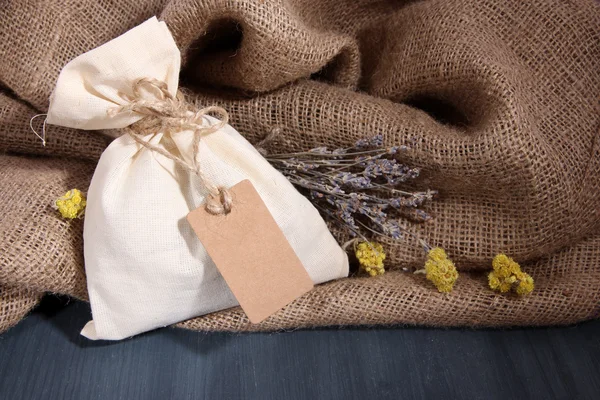 Bolsa de bolsita textil con flores secas, hierbas sobre mesa de madera, sobre fondo de saco — Foto de Stock