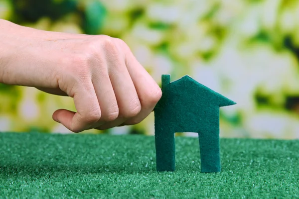 Pequeña casa de papel en la mano sobre hierba verde sobre fondo brillante —  Fotos de Stock