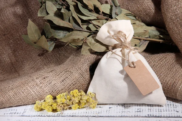 Textile sachet pouch with dried flowers on wooden table, on sackcloth background — Stock Photo, Image