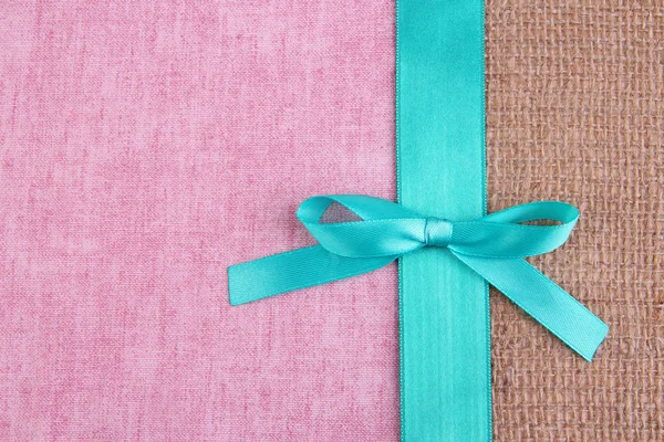 Sackcloth with color ribbon and bow on color fabric background — Stock Photo, Image