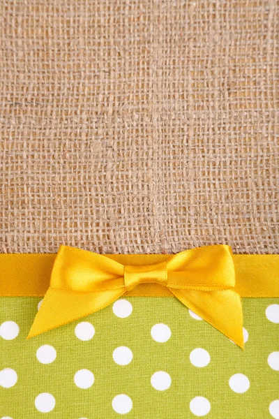 Sackcloth with color ribbon and bow on color fabric background — Stock Photo, Image