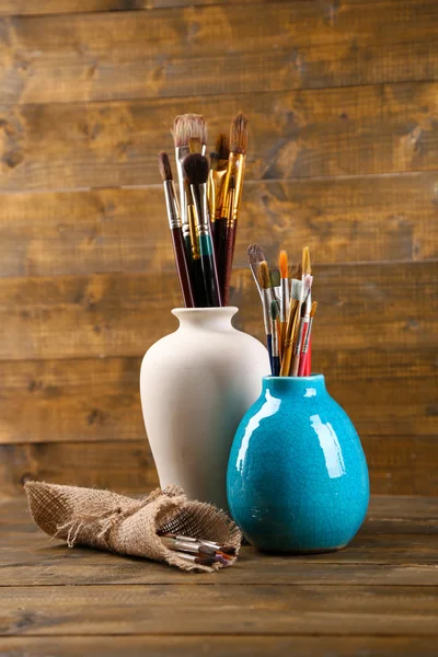 Brushes  in vases on wooden background — Stock Photo, Image