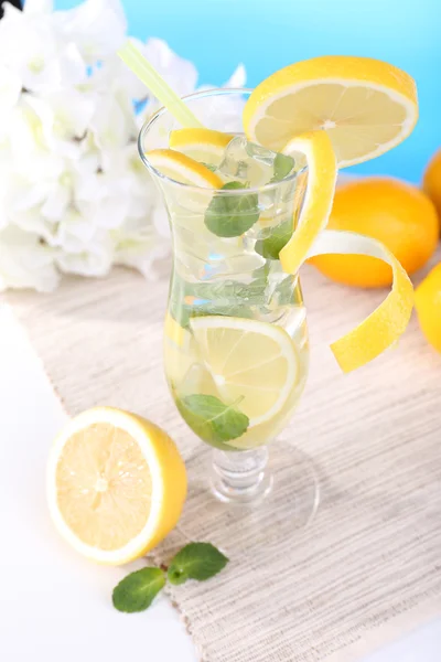Bicchiere di cocktail con limone e menta sul tavolo su sfondo azzurro — Foto Stock