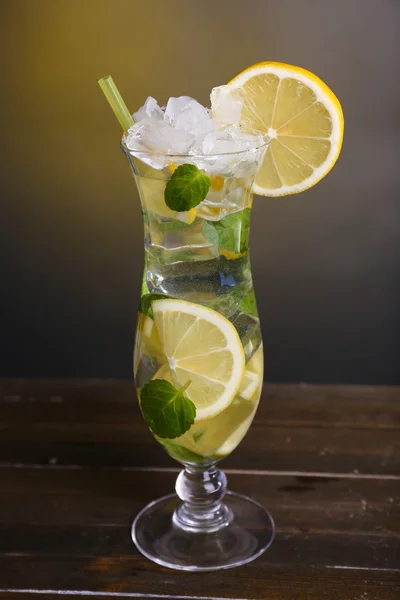 Glass of cocktail with lemon and mint on table on dark yellow background — Stock Photo, Image
