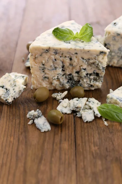 Tasty blue cheese with olives and basil, on wooden table — Stock Photo, Image