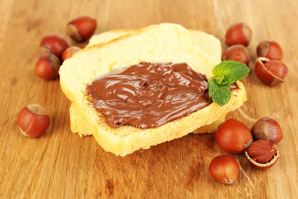 Pane con cioccolato dolce alla nocciola spalmato su fondo di legno — Foto Stock