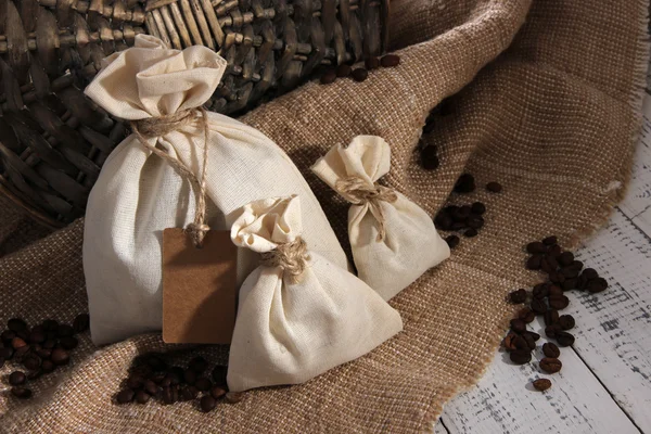 Zakken met koffiebonen op houten tafel, op rouwgewaad achtergrond — Stockfoto