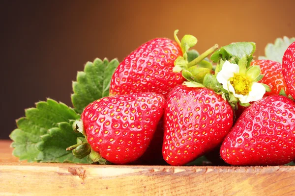 Strawberries with leaves on wooden table on brown  background — Stock Photo, Image